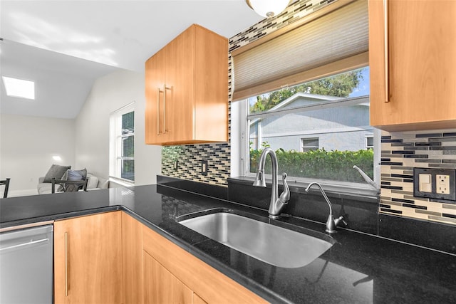 kitchen with stainless steel dishwasher, dark stone counters, sink, and plenty of natural light