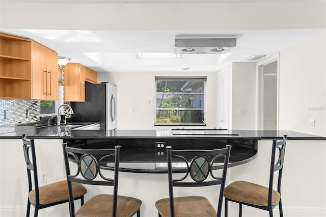 kitchen with kitchen peninsula, a tray ceiling, stainless steel fridge, and tasteful backsplash