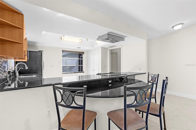 kitchen with tasteful backsplash, kitchen peninsula, sink, stainless steel refrigerator, and light tile patterned floors