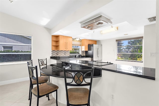 kitchen featuring decorative backsplash, sink, stainless steel fridge, a breakfast bar, and light tile patterned floors