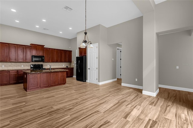 kitchen with black appliances, a kitchen island with sink, light hardwood / wood-style flooring, and hanging light fixtures