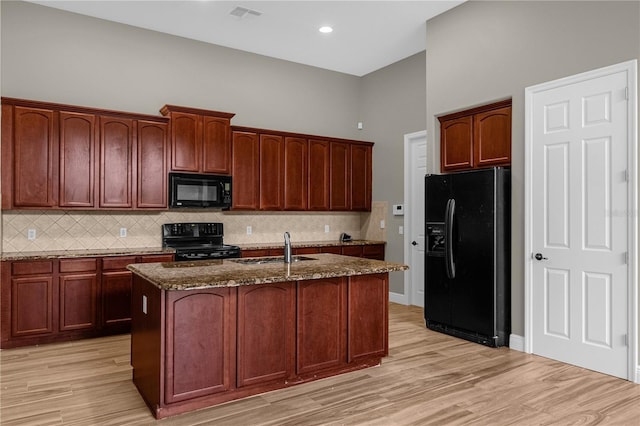 kitchen featuring sink, black appliances, a kitchen island with sink, and stone countertops