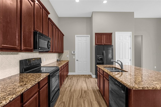 kitchen featuring black appliances, light stone countertops, tasteful backsplash, sink, and a center island with sink