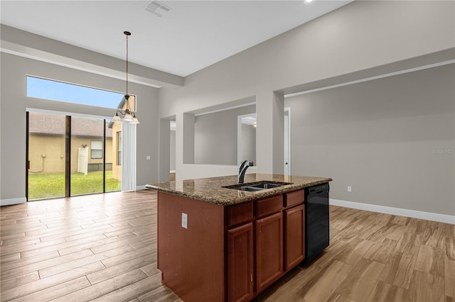 kitchen featuring dishwasher, sink, decorative light fixtures, an island with sink, and dark stone countertops