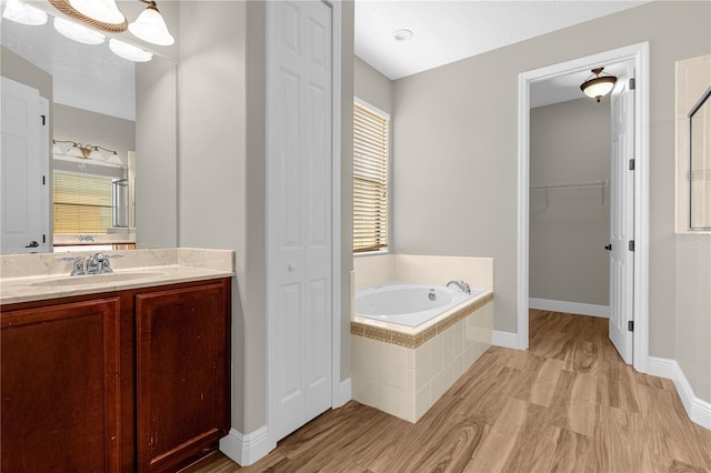 bathroom with wood-type flooring, a relaxing tiled tub, and vanity