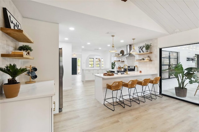 kitchen with a kitchen bar, kitchen peninsula, lofted ceiling, wall chimney range hood, and pendant lighting