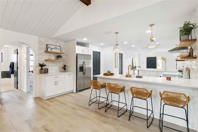 kitchen with white cabinets, stainless steel refrigerator with ice dispenser, decorative light fixtures, vaulted ceiling with beams, and light wood-type flooring