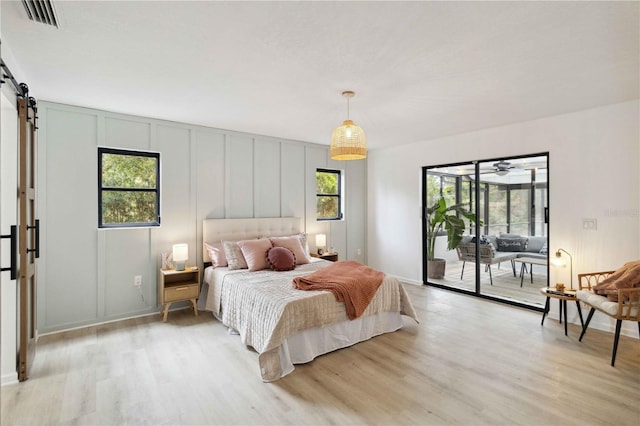 bedroom with access to outside, a barn door, light wood-type flooring, and multiple windows