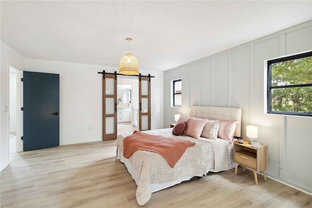 bedroom featuring connected bathroom, light hardwood / wood-style flooring, and a barn door