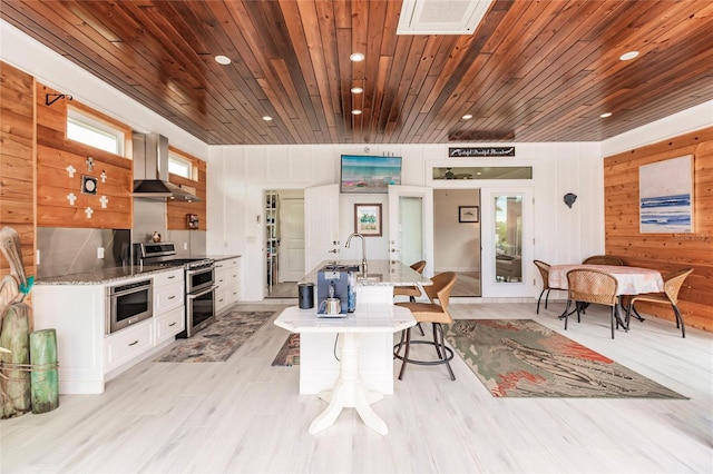 interior space with wall chimney range hood, wood walls, double oven range, white cabinets, and french doors