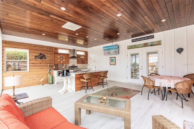 living room with wood ceiling, light hardwood / wood-style floors, wooden walls, french doors, and sink