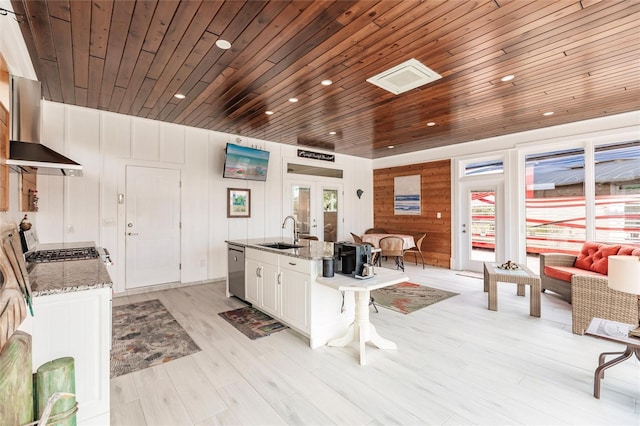 kitchen with wood ceiling, white cabinetry, wall chimney range hood, sink, and light stone counters