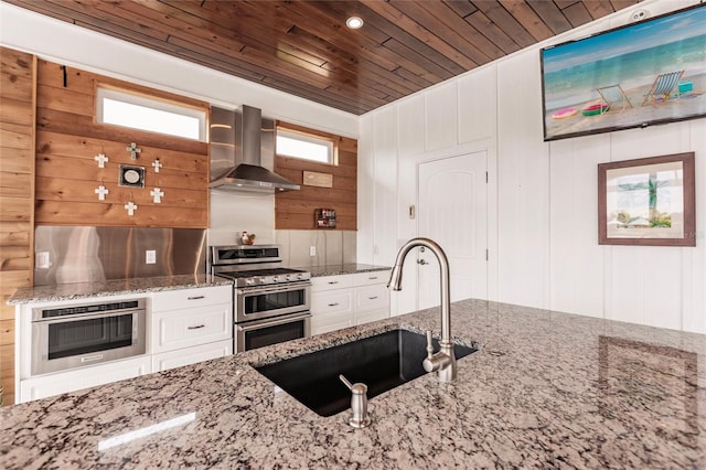 kitchen featuring wall chimney exhaust hood, stainless steel appliances, sink, light stone counters, and wooden ceiling