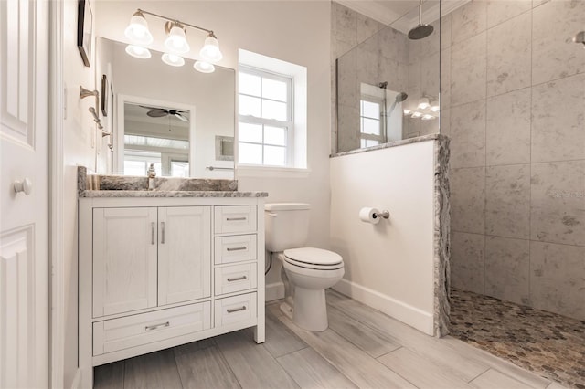 bathroom featuring toilet, ceiling fan, a tile shower, and vanity