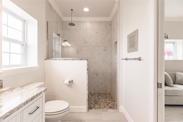 bathroom with a tile shower, vanity, crown molding, and toilet