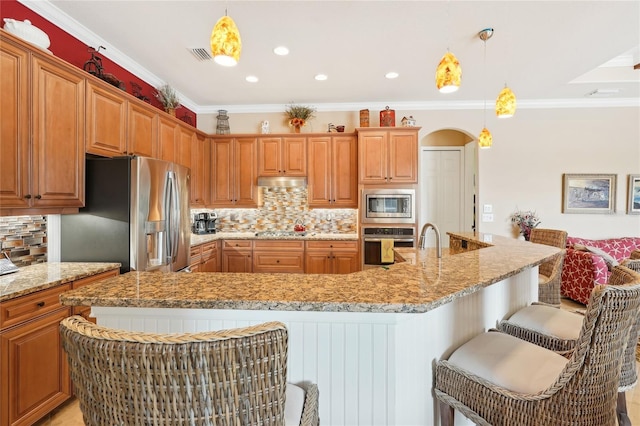 kitchen with appliances with stainless steel finishes, backsplash, hanging light fixtures, ornamental molding, and a breakfast bar