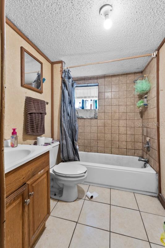 full bathroom featuring toilet, a textured ceiling, tile patterned flooring, shower / bath combination with curtain, and vanity