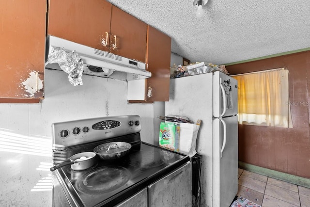 kitchen featuring wooden walls, a textured ceiling, white fridge, light tile patterned floors, and stainless steel electric range