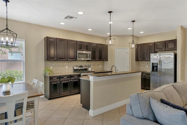 kitchen with light tile patterned floors, a center island with sink, appliances with stainless steel finishes, dark brown cabinets, and pendant lighting