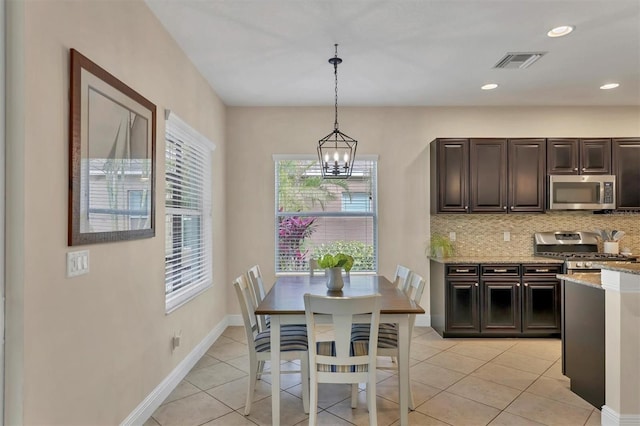 kitchen featuring appliances with stainless steel finishes, dark brown cabinetry, decorative light fixtures, light stone counters, and light tile patterned floors