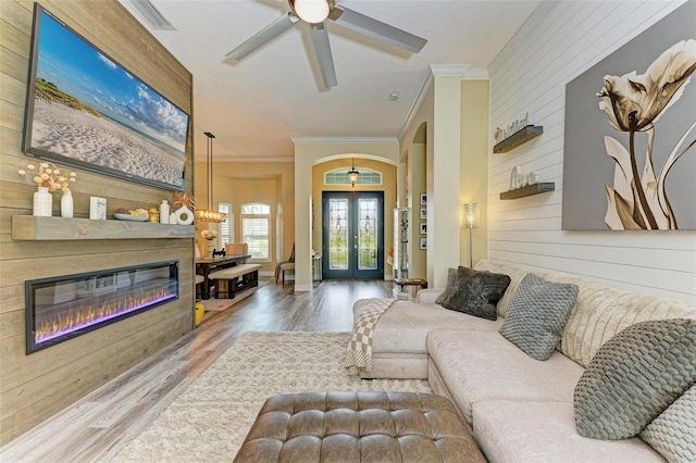 living room with ceiling fan, wood walls, hardwood / wood-style flooring, ornamental molding, and french doors