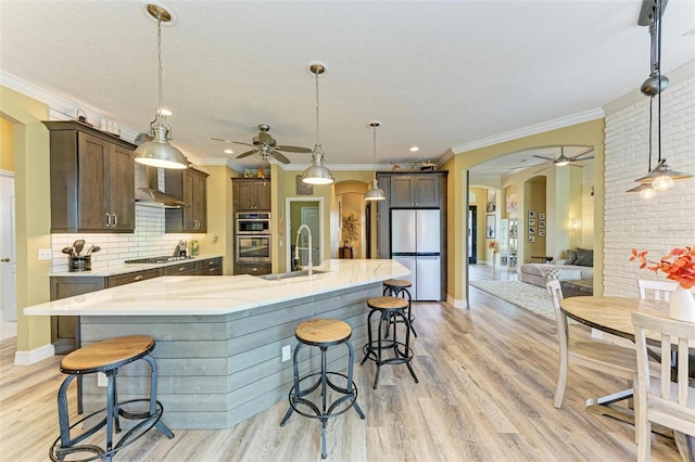 kitchen with a large island with sink, stainless steel appliances, sink, hanging light fixtures, and dark brown cabinets