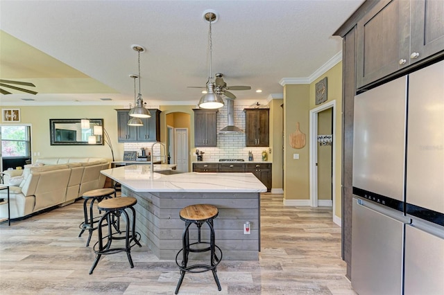 kitchen featuring a kitchen bar, a spacious island, decorative light fixtures, wall chimney range hood, and sink