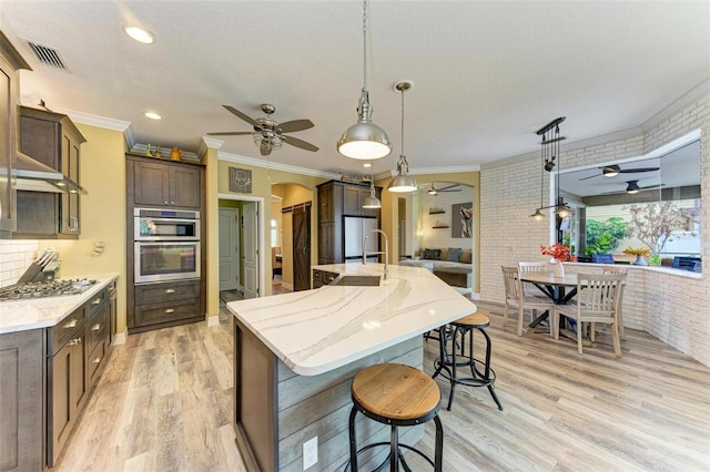 kitchen featuring decorative light fixtures, light hardwood / wood-style floors, a large island, dark brown cabinets, and brick wall