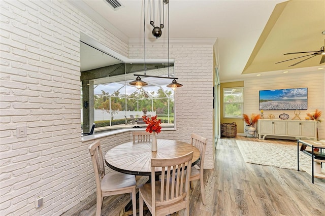 dining area with ceiling fan, brick wall, ornamental molding, and light hardwood / wood-style flooring