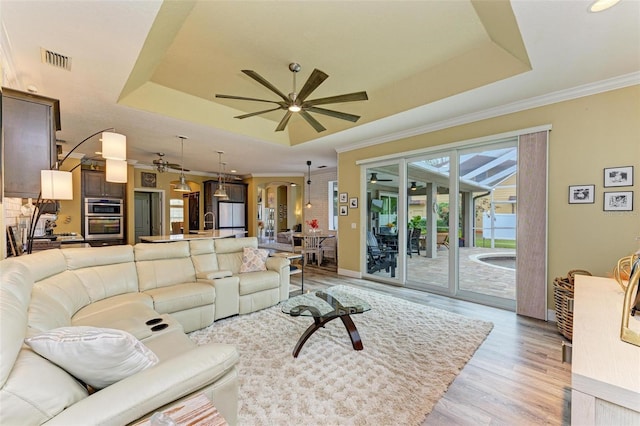 living room with sink, a tray ceiling, crown molding, and light wood-type flooring