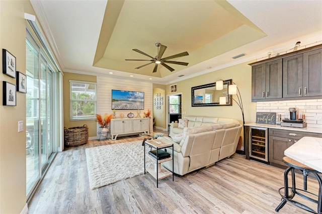 living room with light hardwood / wood-style floors, ceiling fan, a raised ceiling, beverage cooler, and ornamental molding