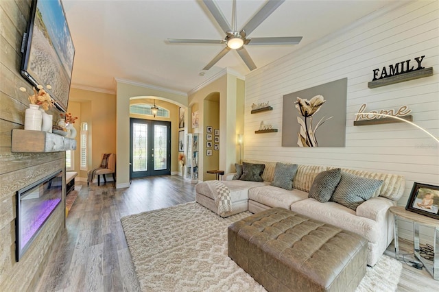 living room featuring wood walls, ceiling fan, wood-type flooring, french doors, and crown molding