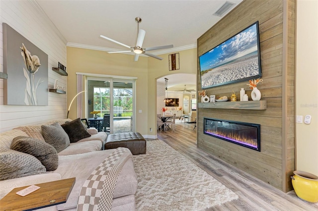 living room featuring ceiling fan, a fireplace, crown molding, and light hardwood / wood-style floors