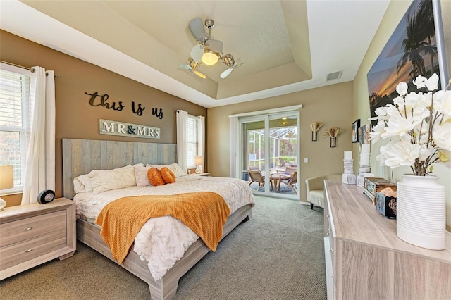 carpeted bedroom with a raised ceiling, access to exterior, ceiling fan with notable chandelier, and multiple windows