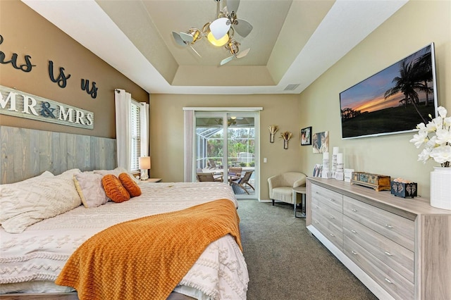 bedroom featuring ceiling fan with notable chandelier, a tray ceiling, access to outside, and dark colored carpet