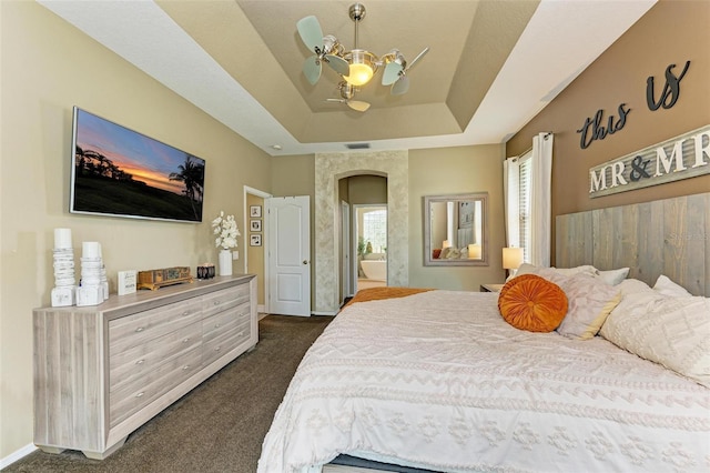 bedroom with ceiling fan, a tray ceiling, and dark carpet