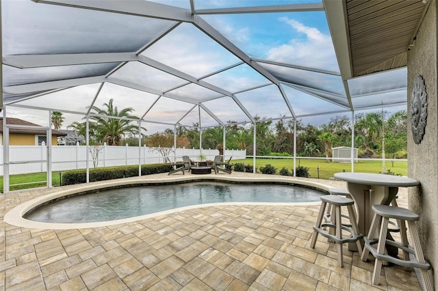 view of swimming pool featuring glass enclosure, a shed, and a patio