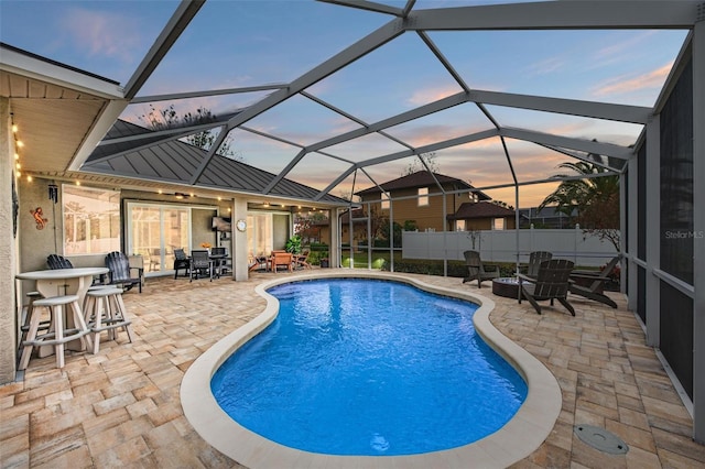 pool at dusk with a patio area and glass enclosure