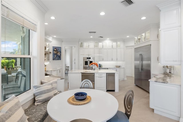 kitchen featuring stainless steel appliances, light tile patterned flooring, hanging light fixtures, crown molding, and white cabinets