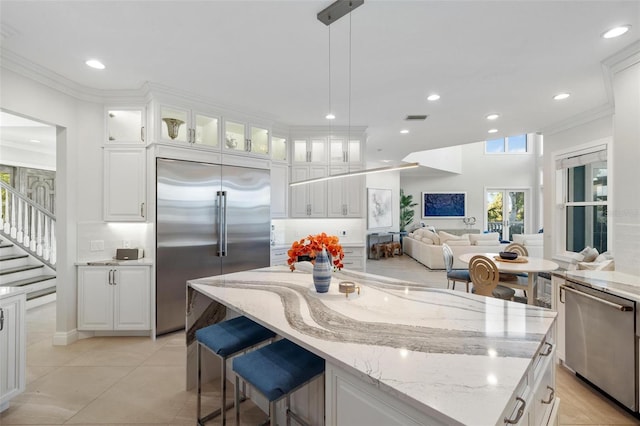 kitchen with light tile patterned floors, white cabinetry, stainless steel appliances, decorative light fixtures, and light stone counters