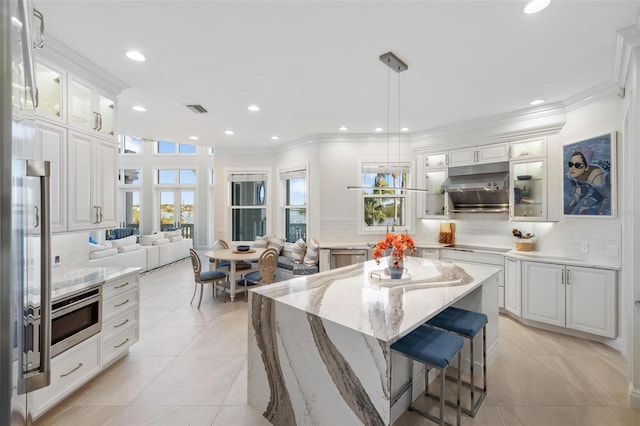 kitchen with tasteful backsplash, a center island, white cabinetry, hanging light fixtures, and light tile patterned floors