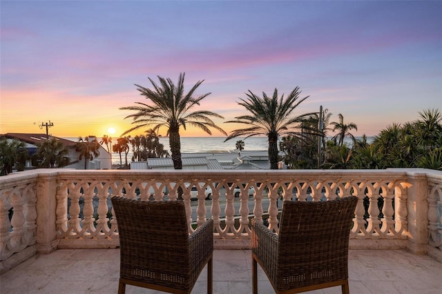 balcony at dusk featuring a water view