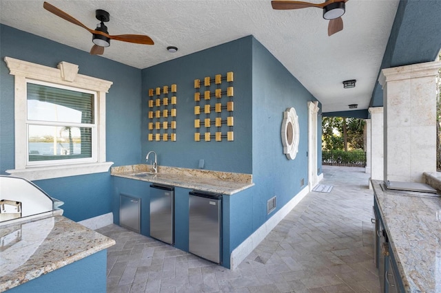 interior space with a textured ceiling, refrigerator, blue cabinets, and sink