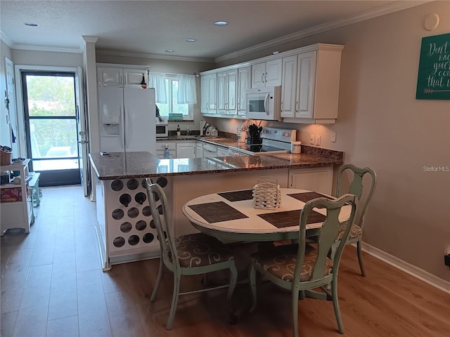 kitchen featuring white appliances, white cabinetry, dark stone countertops, kitchen peninsula, and light wood-type flooring