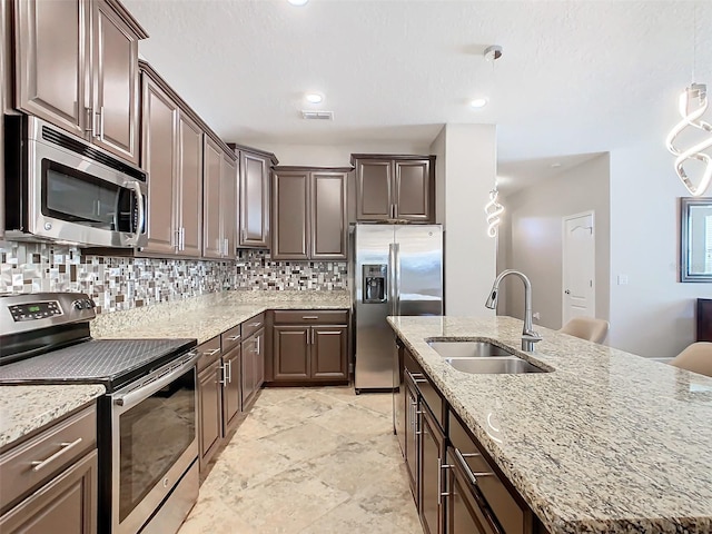 kitchen featuring tasteful backsplash, an island with sink, sink, stainless steel appliances, and dark brown cabinets