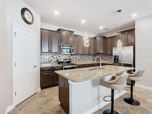 kitchen featuring a kitchen bar, sink, decorative light fixtures, appliances with stainless steel finishes, and an island with sink