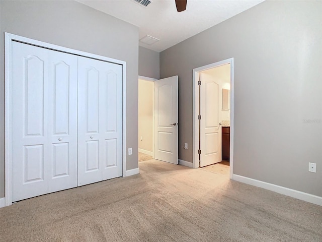 unfurnished bedroom with light colored carpet, a closet, ceiling fan, and ensuite bathroom