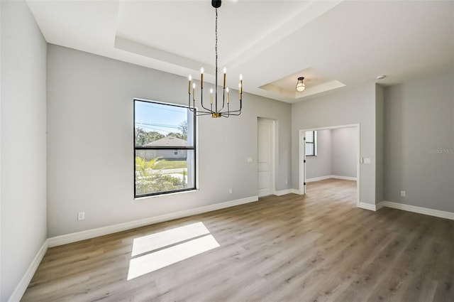 unfurnished dining area with wood-type flooring, a raised ceiling, and a chandelier