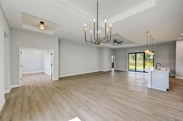 unfurnished living room featuring sink, a tray ceiling, light hardwood / wood-style floors, and ceiling fan