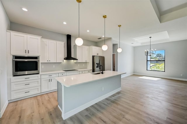 kitchen featuring white cabinets, stainless steel appliances, decorative light fixtures, and wall chimney range hood